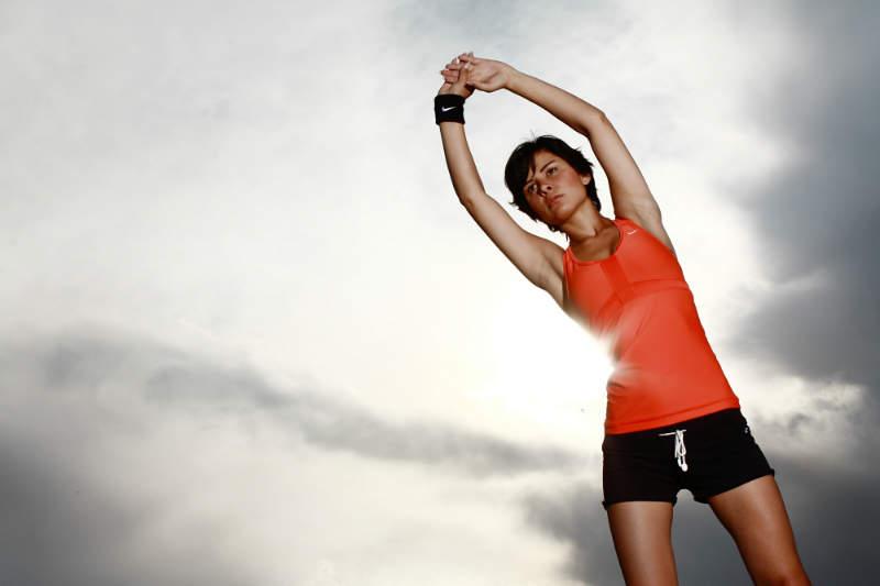 sportswoman stretching clouds sunburst